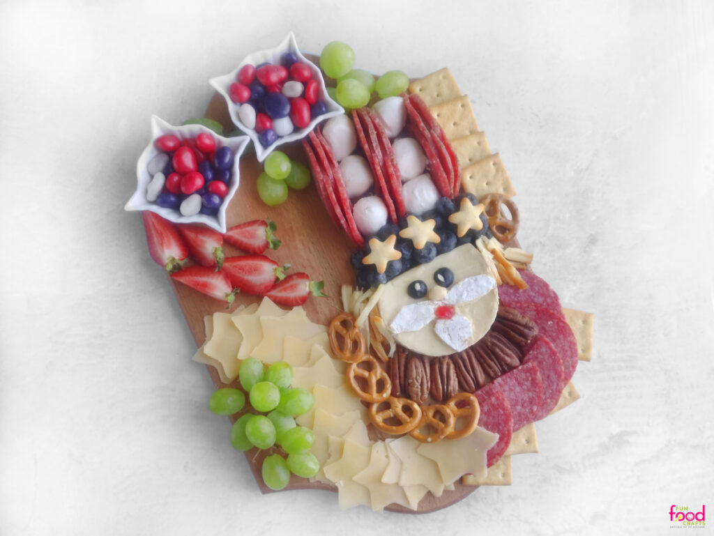 Uncle Sam Charcuterie Board nearly complete with added strawberries, grapes, crackers, cheese stars, and pretzels in a festive red, white, and blue layout.
