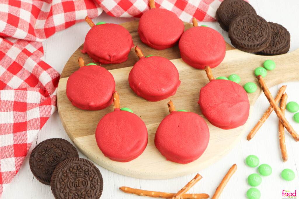 Overhead image of Apple Oreo cookies made by dipping Oreos in red melted chocolate and using pretzel sticks for the stems and green candies for the leaves