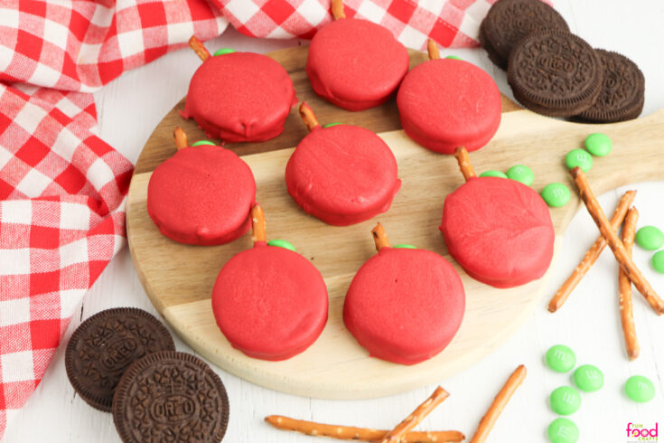 Overhead image of Apple Oreo cookies made by dipping Oreos in red melted chocolate and using pretzel sticks for the stems and green candies for the leaves