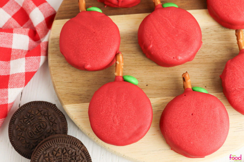 two Oreos next to red-chocolate-dipped Oreos with pretzel stick stems and green candy leaves made into a cute Fall apple-themed snack