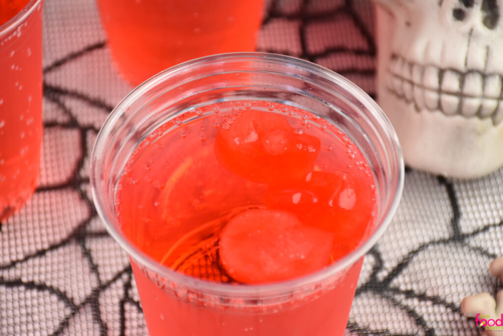 close up of cherry ice skulls for Halloween drinks floating in a glass of soda slowly melting and coloring and flavoring the drink a cherry-flavored red