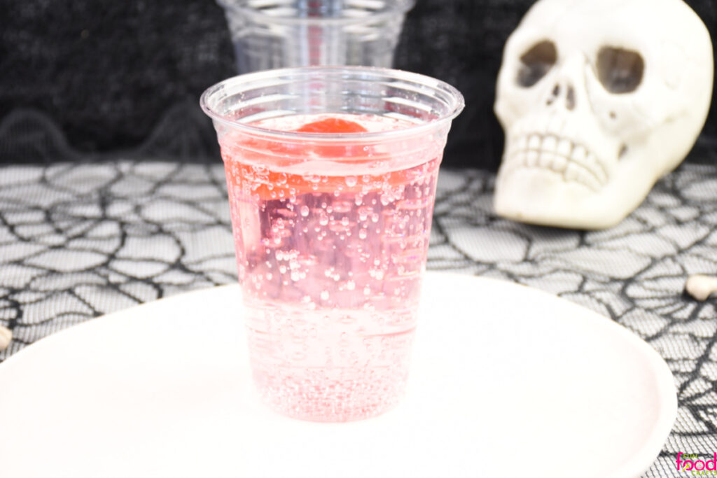 Ice skulls added to a glass of clear soda just beginning to melt and color the soda red