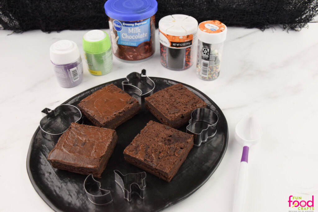 Ingredients for Halloween Sprinkle Brownies including store-bought brownies, frosting, Halloween sprinkles, and cookie cutters on a white background.