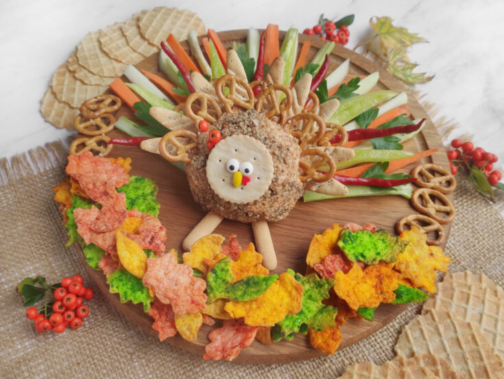 Festive turkey cheese ball centerpiece made with cream cheese nuts pretzels and fresh veggies for a fun Thanksgiving snack