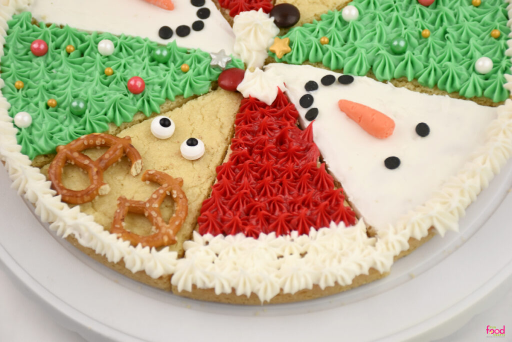 Top view of a decorated Christmas sugar cookie pizza featuring pretzel antlers, star sprinkles, and piped icing details.