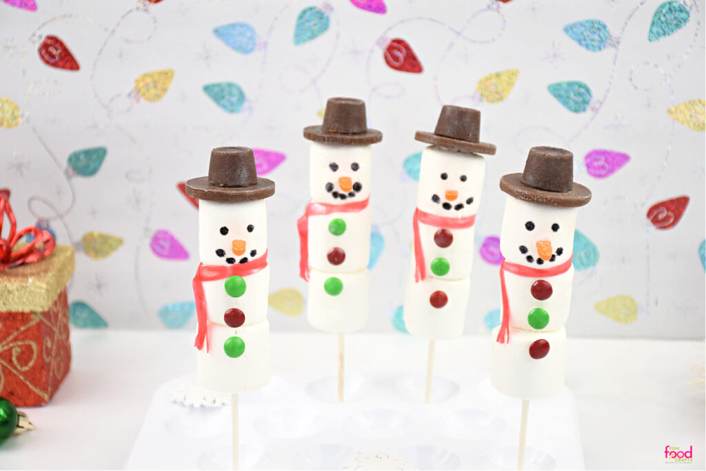 A group of four finished snowman marshmallow pops sitting in a cake pop holder