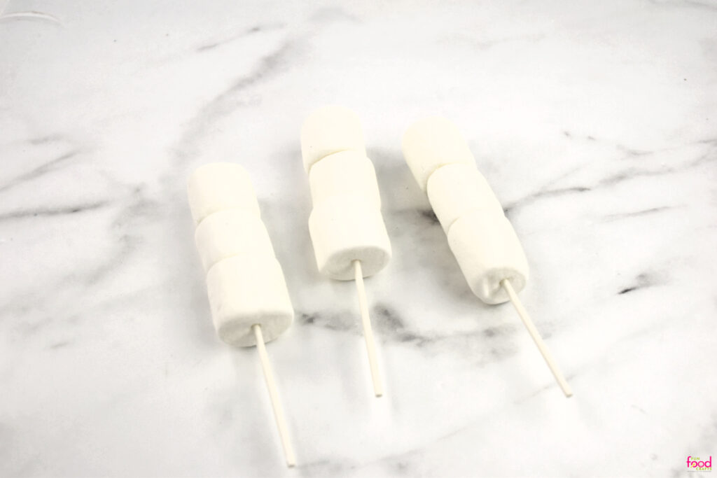 Adding three marshmallows to a lollipop stick to form the snowman's body