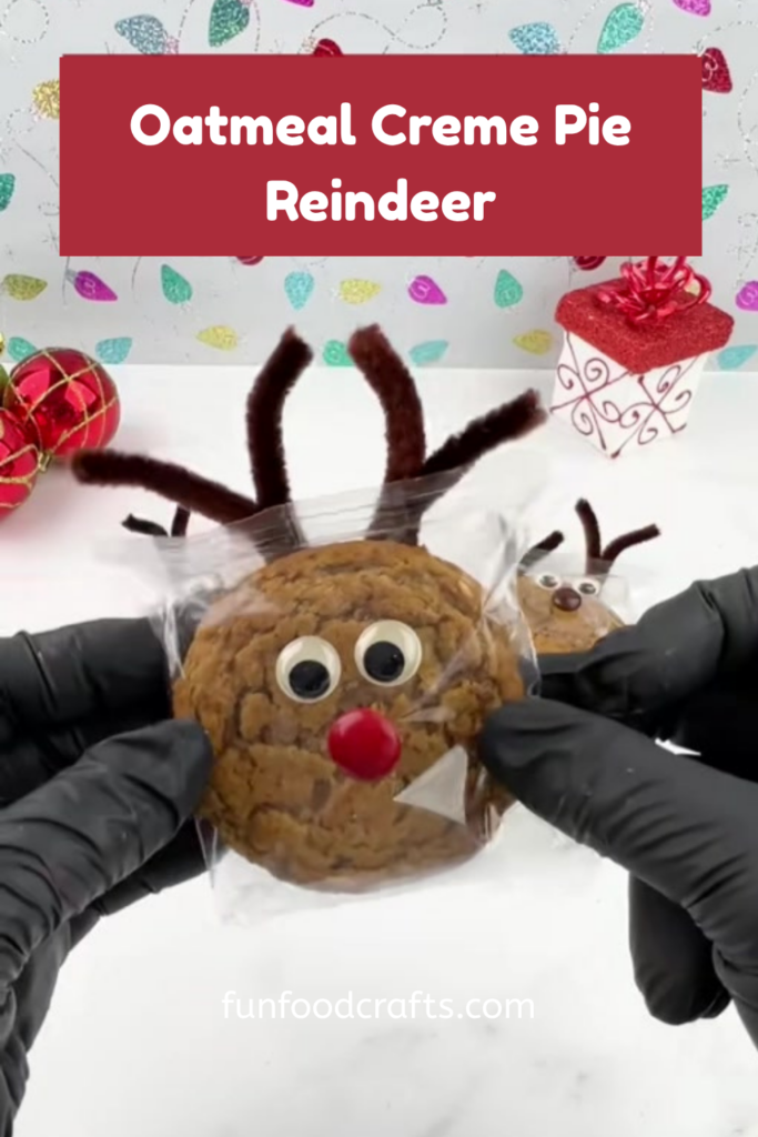 Hand holding an oatmeal creme pie reindeer with googly eyes, pipe cleaner antlers, and a red M&M nose on the wrapper.